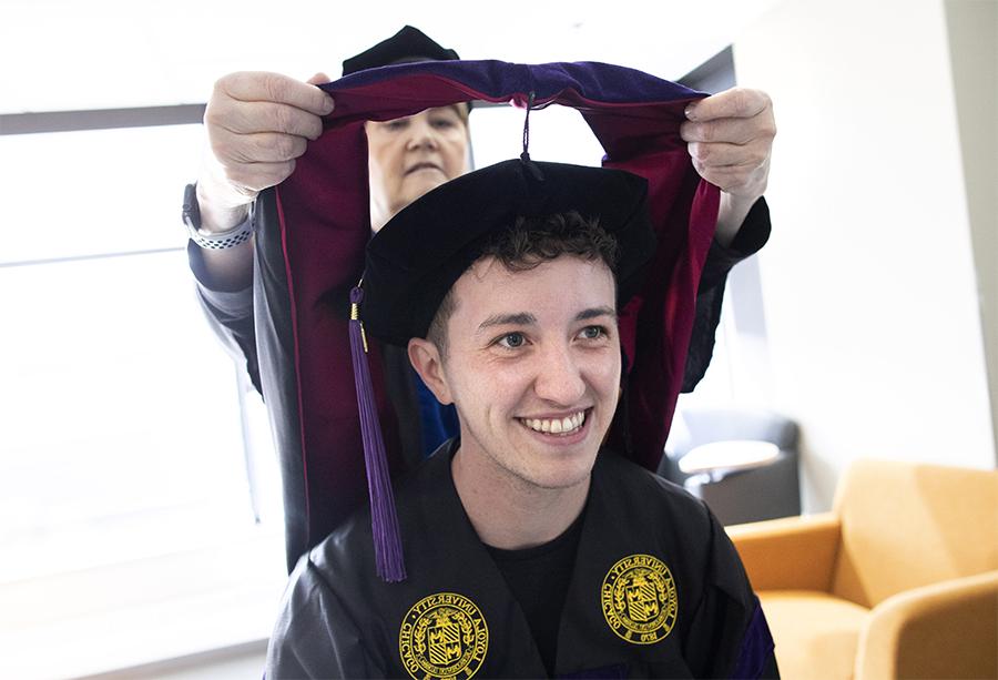 A faculty member places an academic hood on a smiling student.