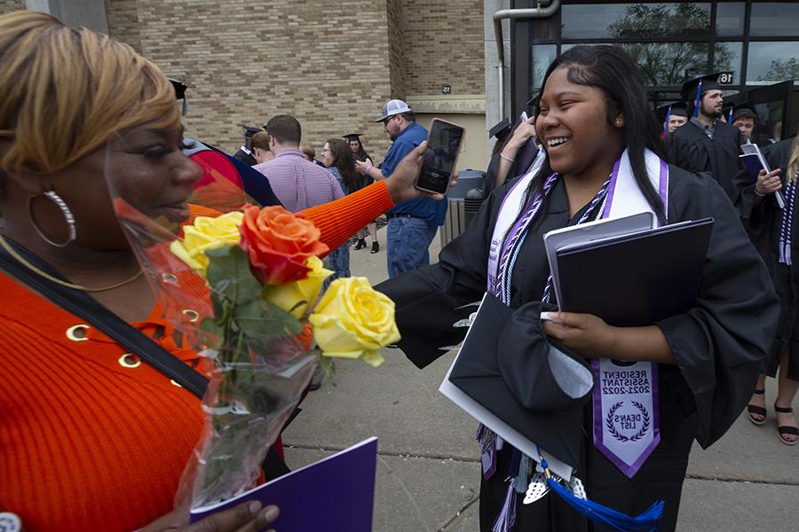 A student holds their diploma and smiles at graduation with their family.