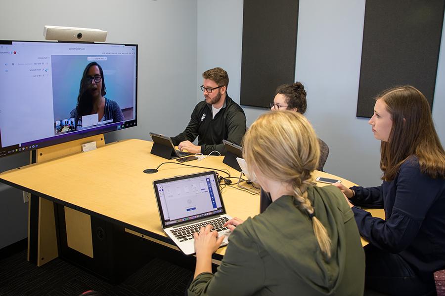 Students sit around a table and participate on a video call.