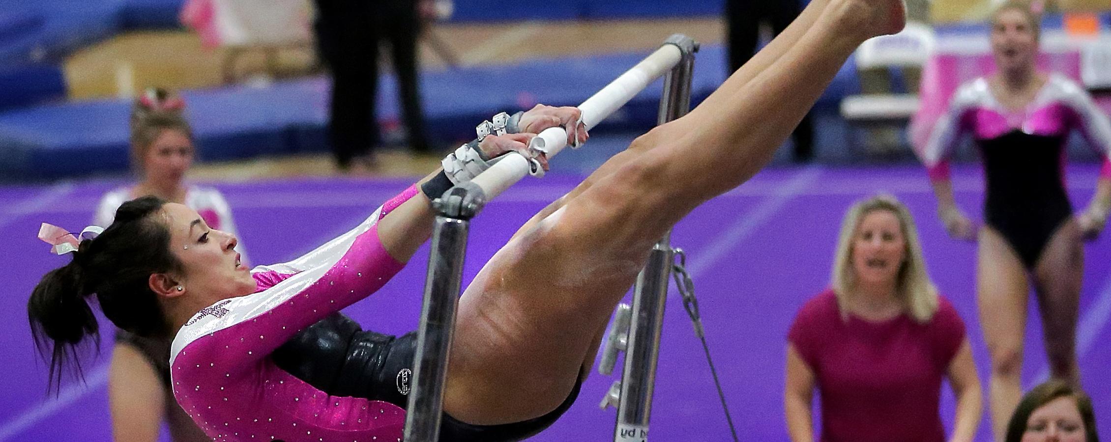 A Warhawk gymnast with a look of determination is encouraged by a coach and a teammate.