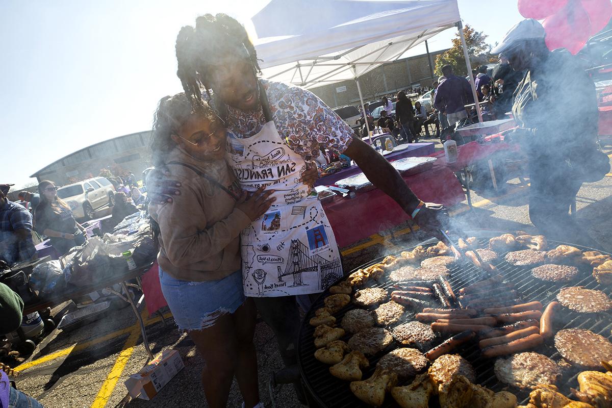 A picture of tailgating in the parking lot with lots of cars, pop-up tents and grills.