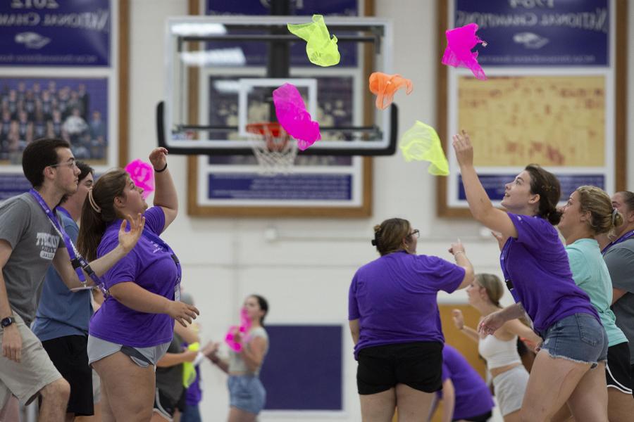 Students face each other in two lines and toss colorful objects back and forth.