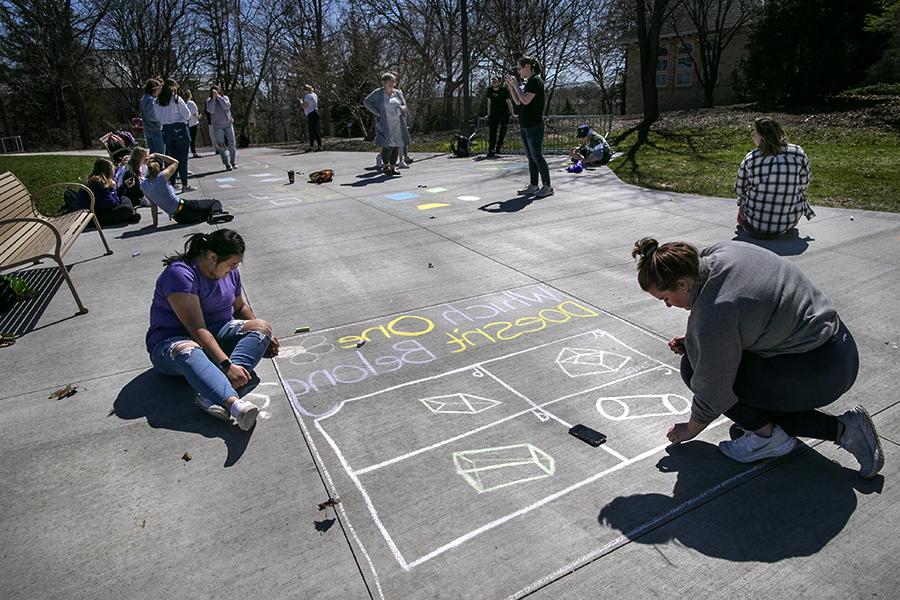 Students write math problems on a sidewalk with challk.