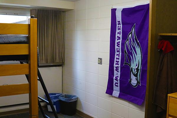 A dorm room. The left side has 2 trash cans and a UW Whitewater flag, and the right side has a lofted bed.