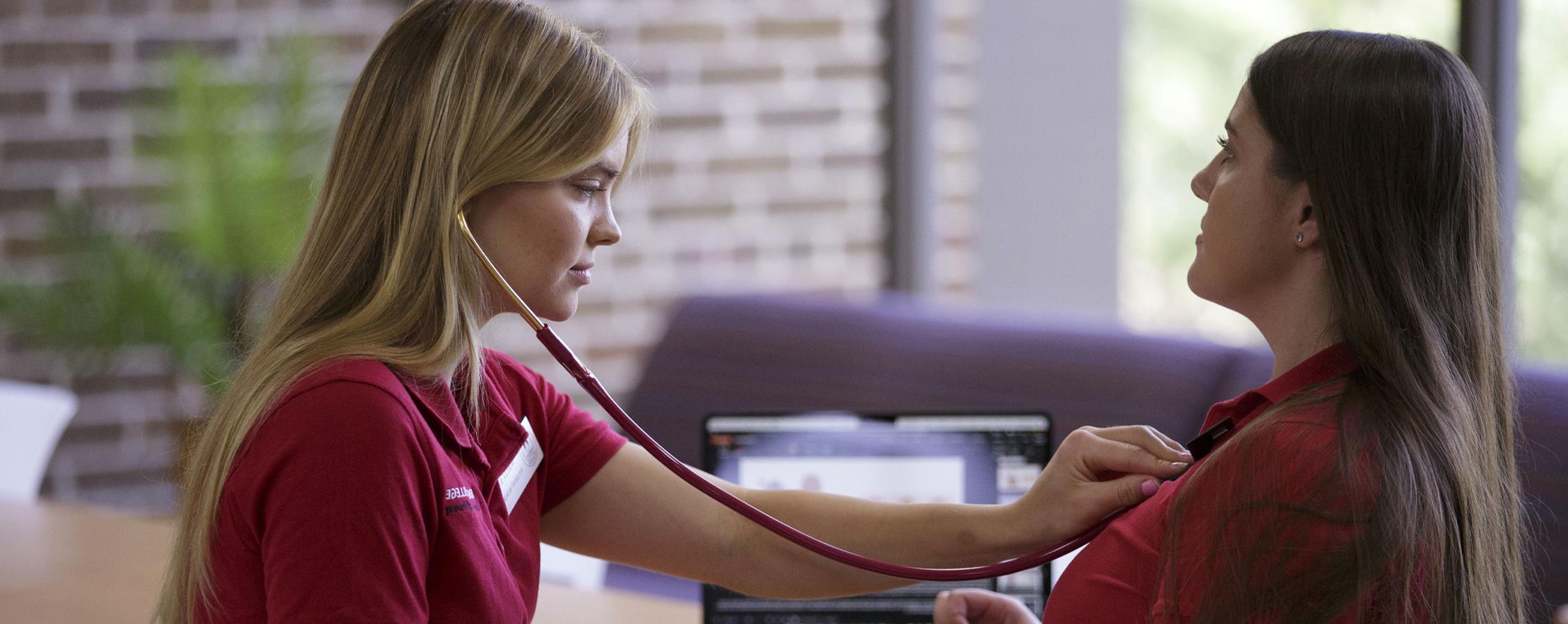 A student uses a stethoscope to listen to another student's chest.